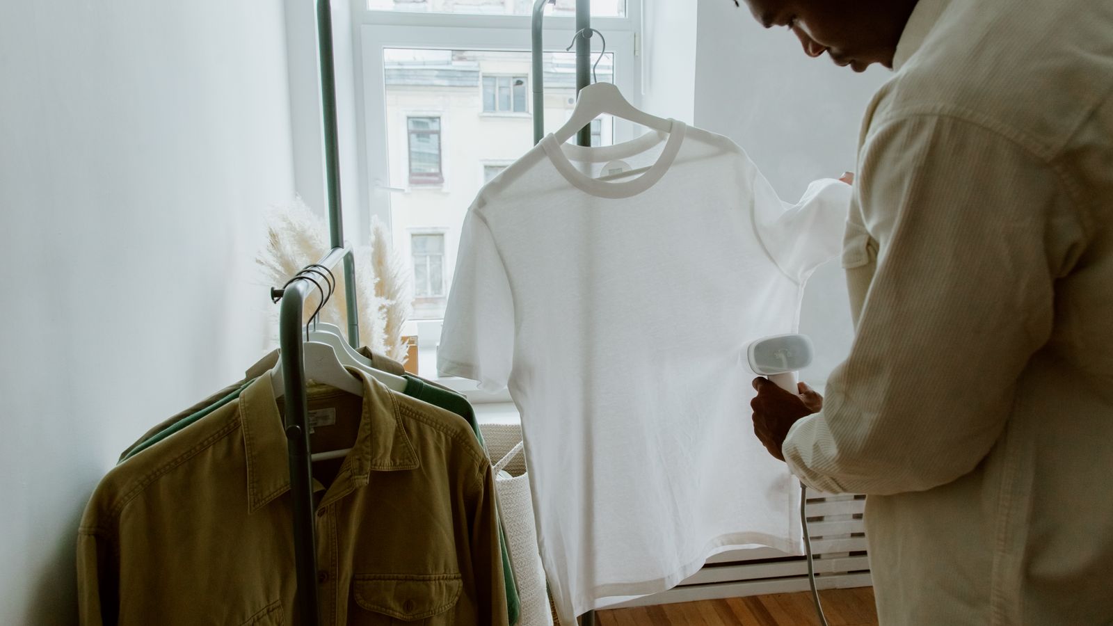 A man steaming a white shirt hanging on a clothing rack indoors