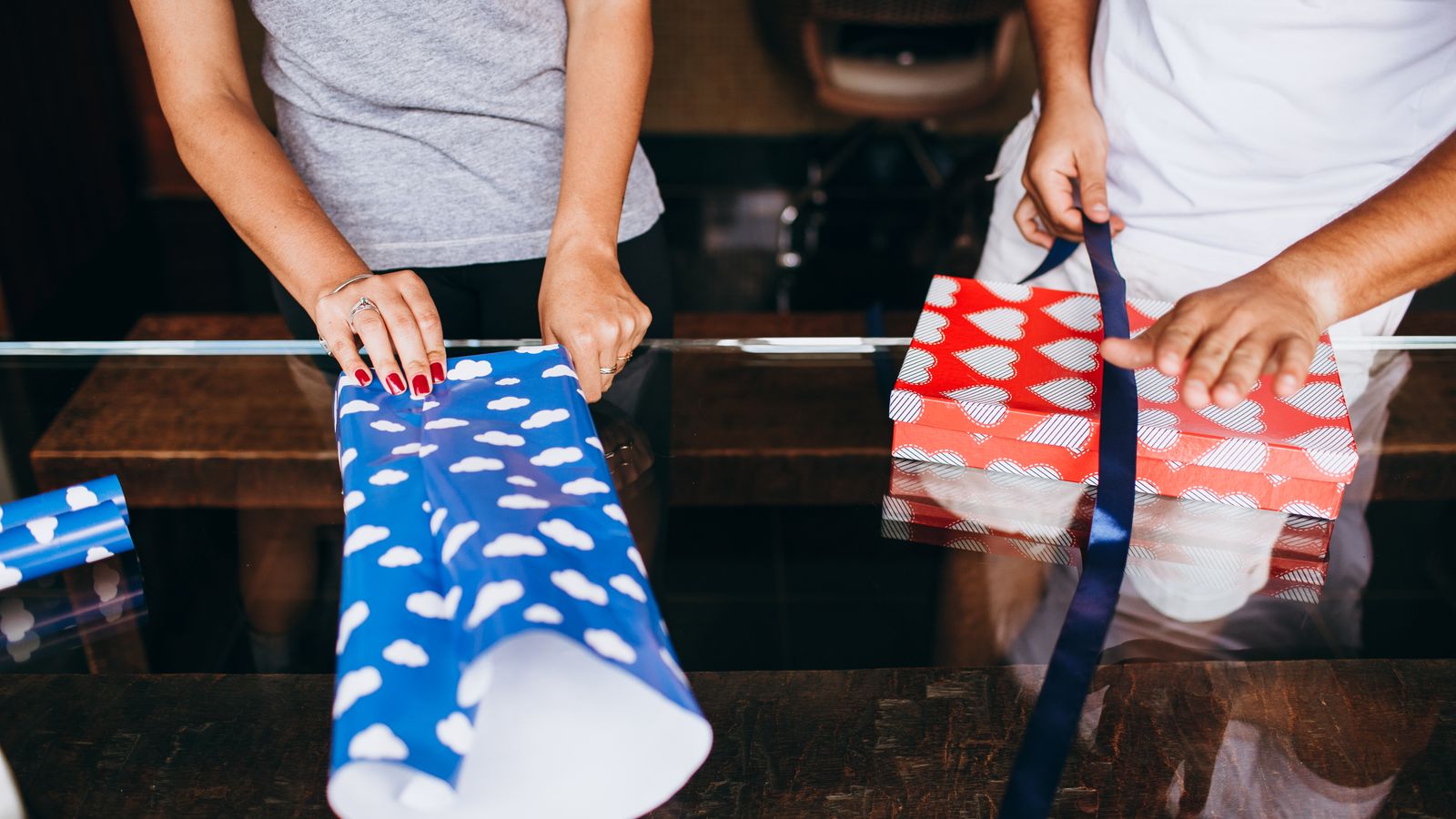 Two adults wrapping gifts with colorful paper and ribbons indoors