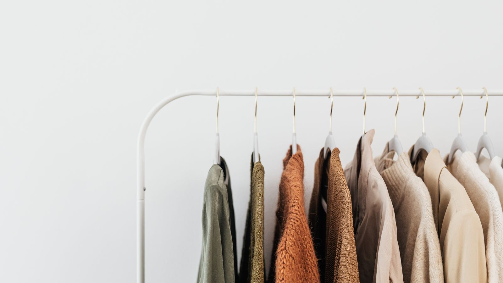 A minimalist clothing rack displaying neutral toned outfits in a tidy room
