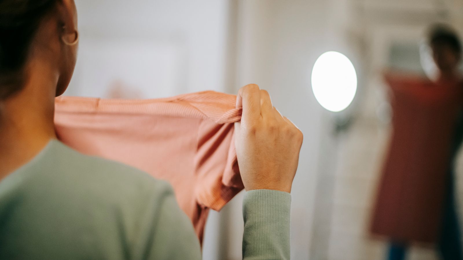 A woman holding a pink dress in front of a mirror at home