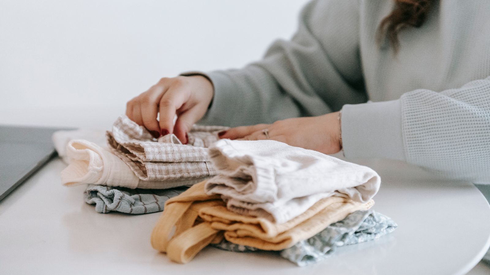 A woman folding colorful baby clothes at a white table at home