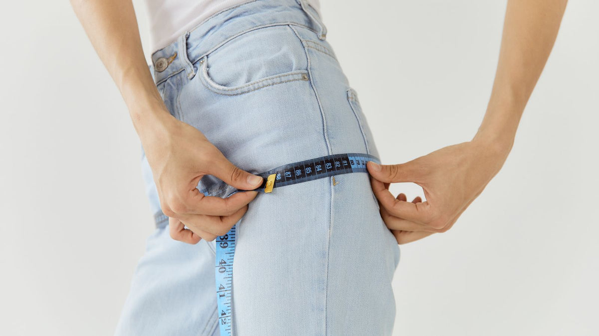 Person measuring the hips of light blue jeans with a blue tape measure