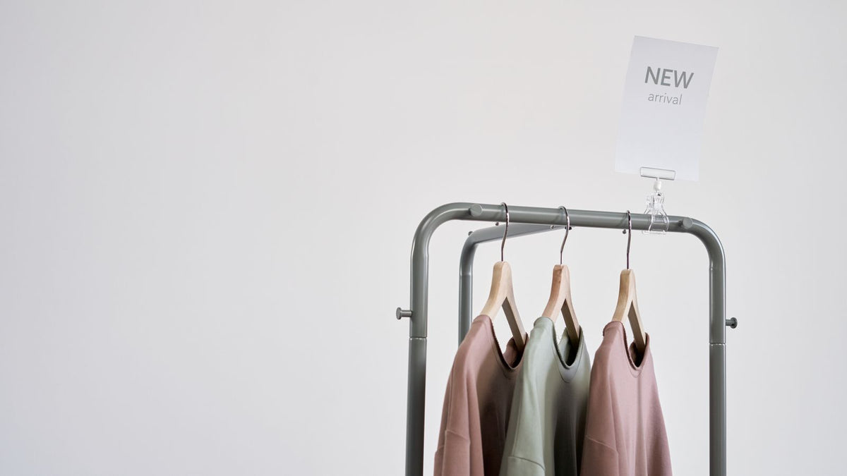 A rack of clothing beside a New Arrival sign on a white wall
